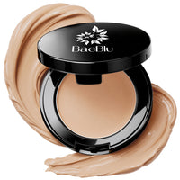 An open black BaeBlu concealer compact with a beige/tan concealer inside, surrounded by decorative swirled makeup smears on a white background.