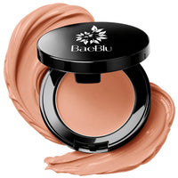 An open black BaeBlu concealer compact with a beige concealer inside, surrounded by decorative swirled makeup smears on a white background.